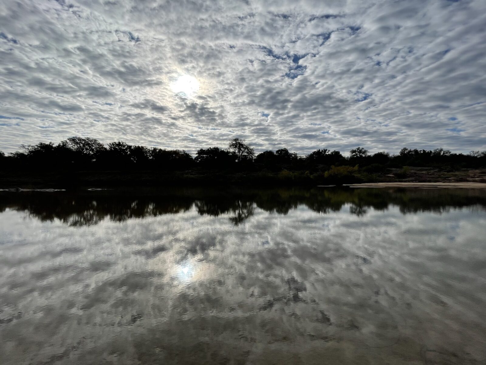 reflection of cloudy sky over trees and water